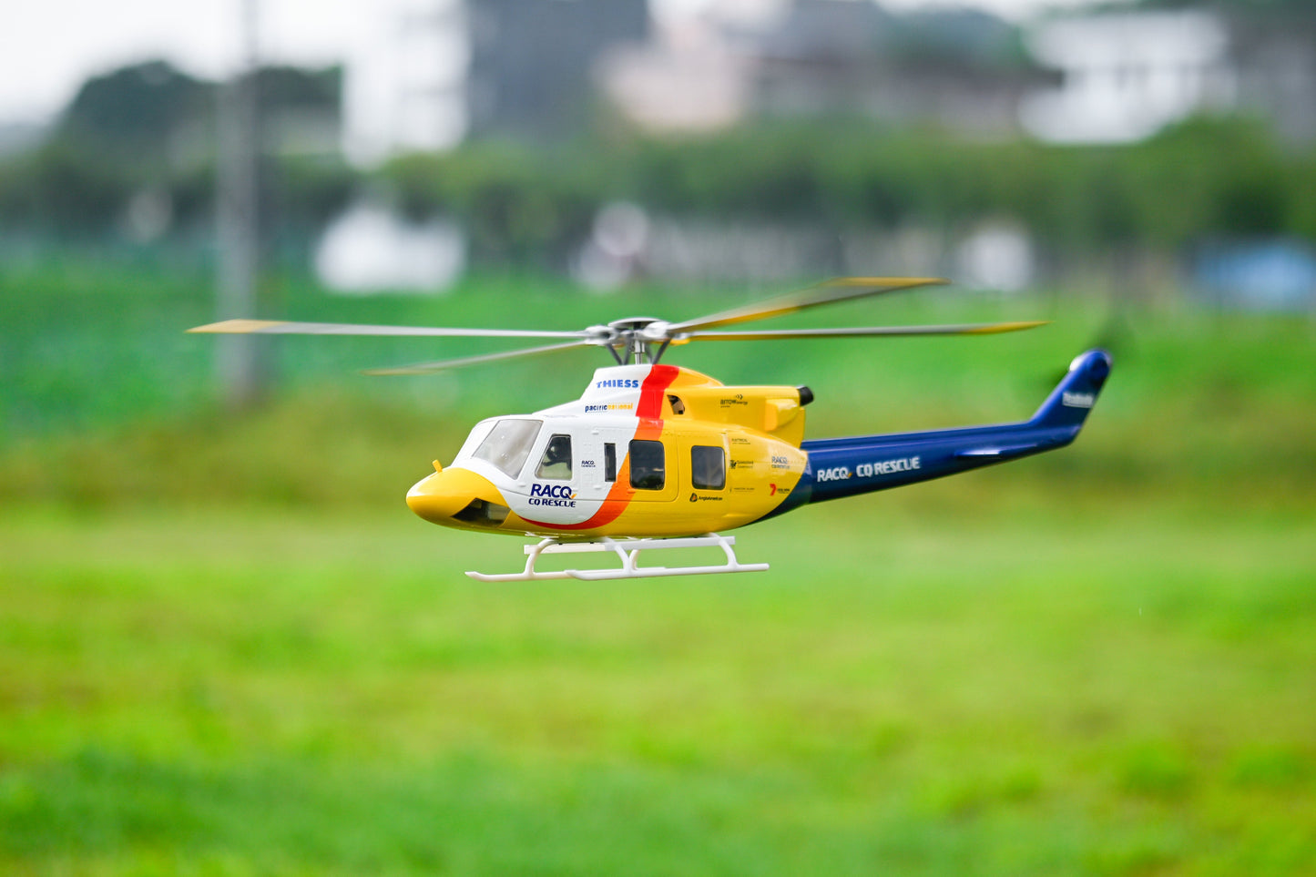Model helicopter flying over a grassy field with blurred background
